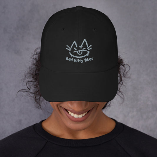 Woman wearing a black cap with a design of a cat's face and the words 'Bad Kitty Vibes'.