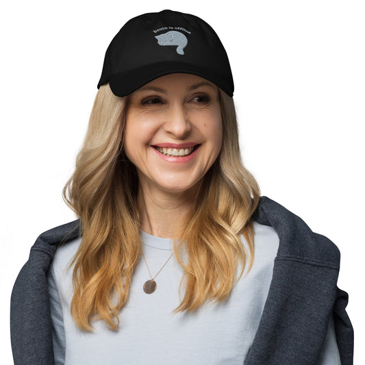 Woman wearing a black cap with a design of a cat hiding its face and the words 'Brain is Offline'.