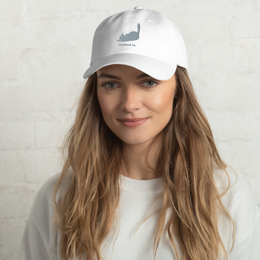 Woman wearing a white cap with a design of a pouncing cat and the words "Locked In".