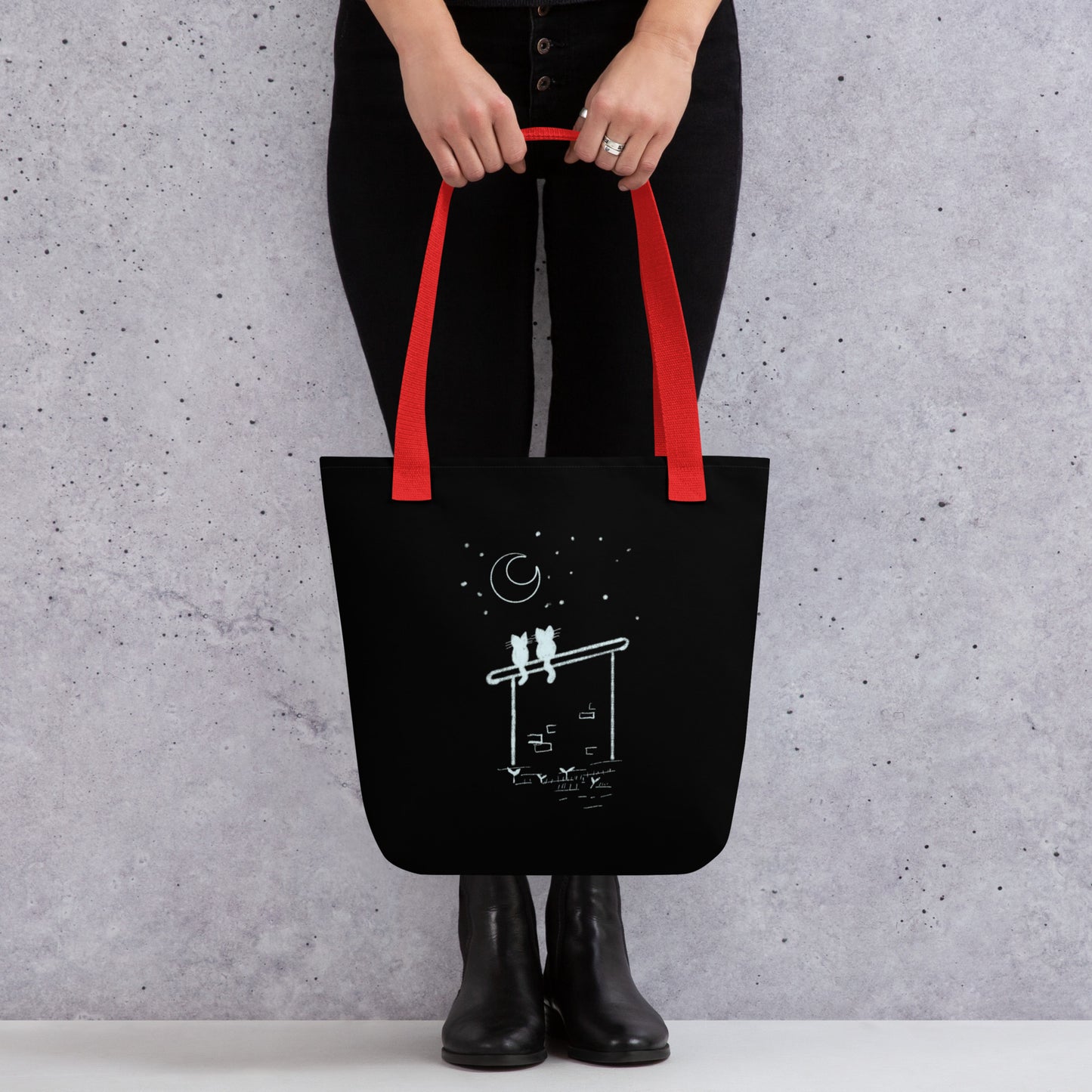 Front View of a black tote bag with a design of two stargazing cats. Red Handle.