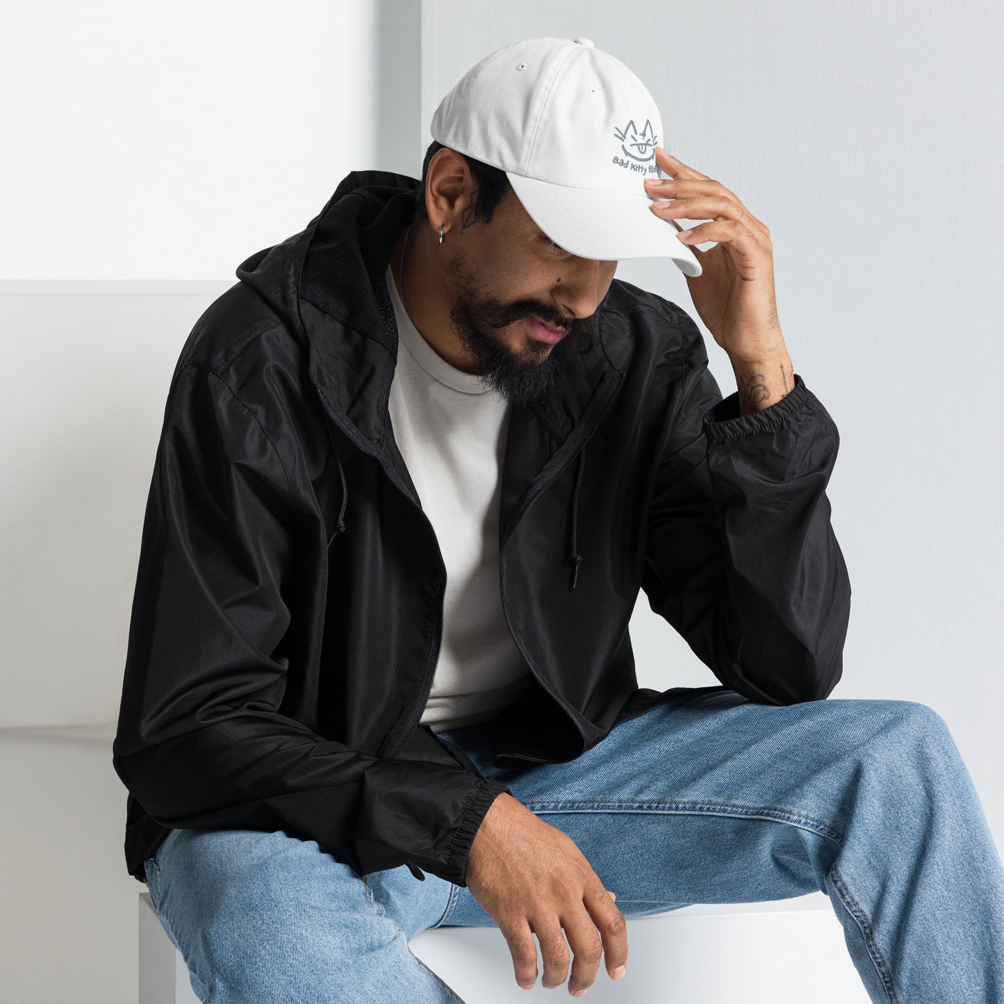 Man wearing a white cap with a design of a cat's face and the words 'Bad Kitty Vibes'.