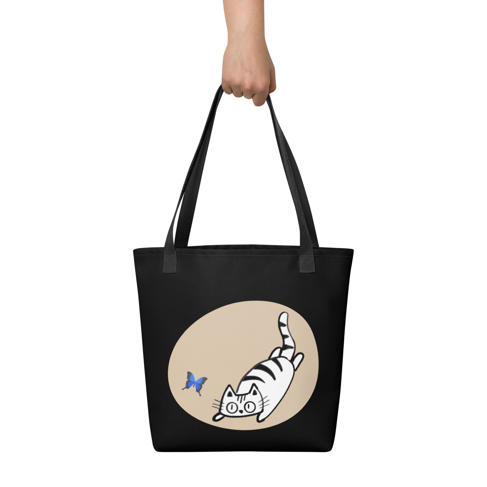 Front View of a tote bag with a design of a cat chasing a butterfly. Black Handle.