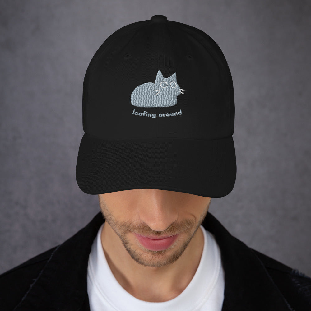 Man wearing a black cap with a design of a cat relaxing and the words "Loafing Around".