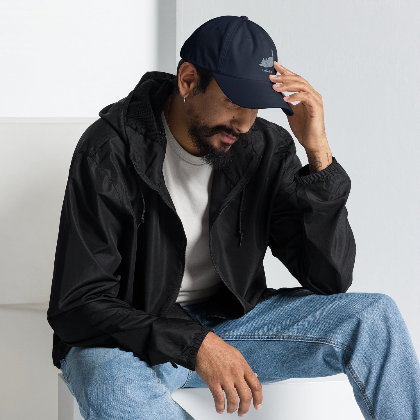 Man wearing a navy cap with a design of a pouncing cat and the words "Locked In".