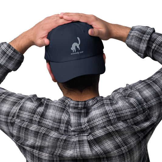 Man wearing a navy cap with a design of a scared cat with the words "Scaredy Cat".