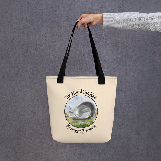 Front View of a tote bag with a design of a cat sleeping in a field of flowers with the words "The World Can Wait. Black Handle.