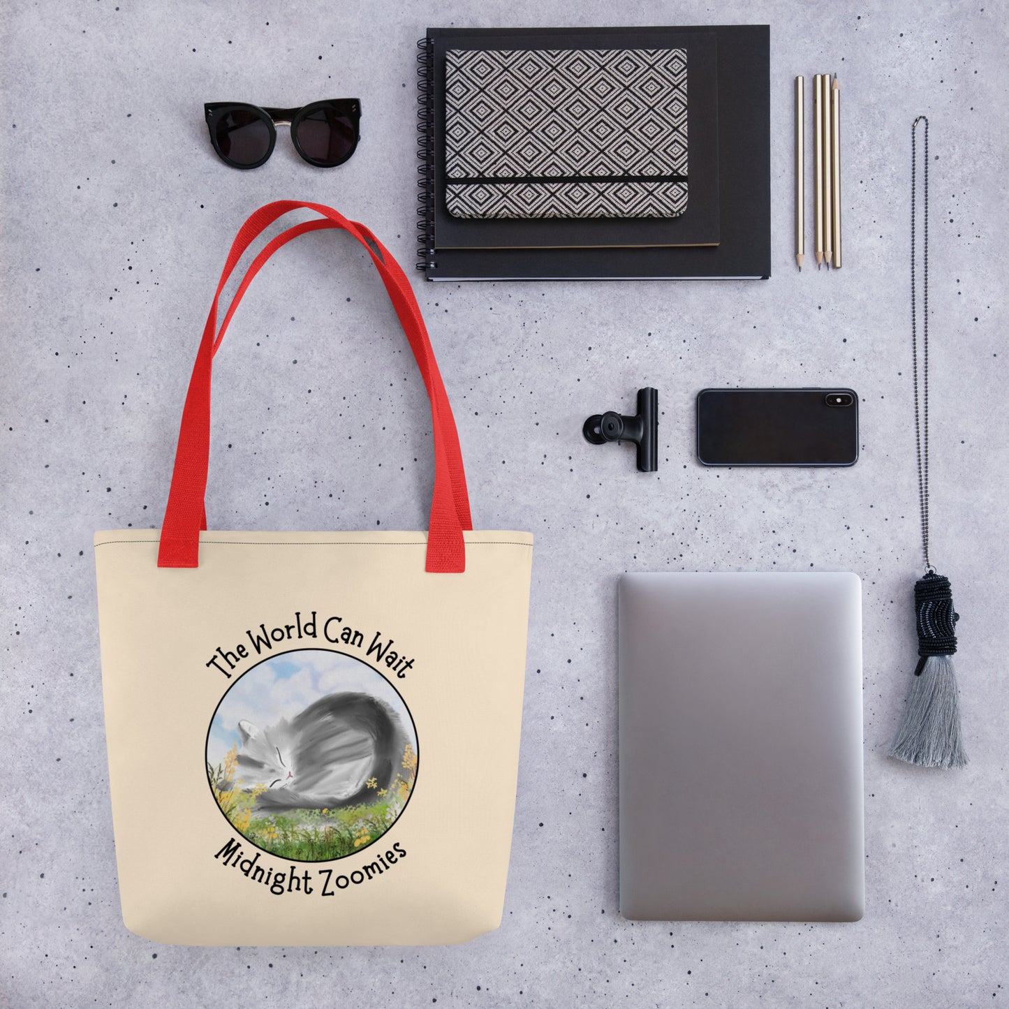 Front View of a tote bag with a design of a cat sleeping in a field of flowers with the words "The World Can Wait. Red Handle.   