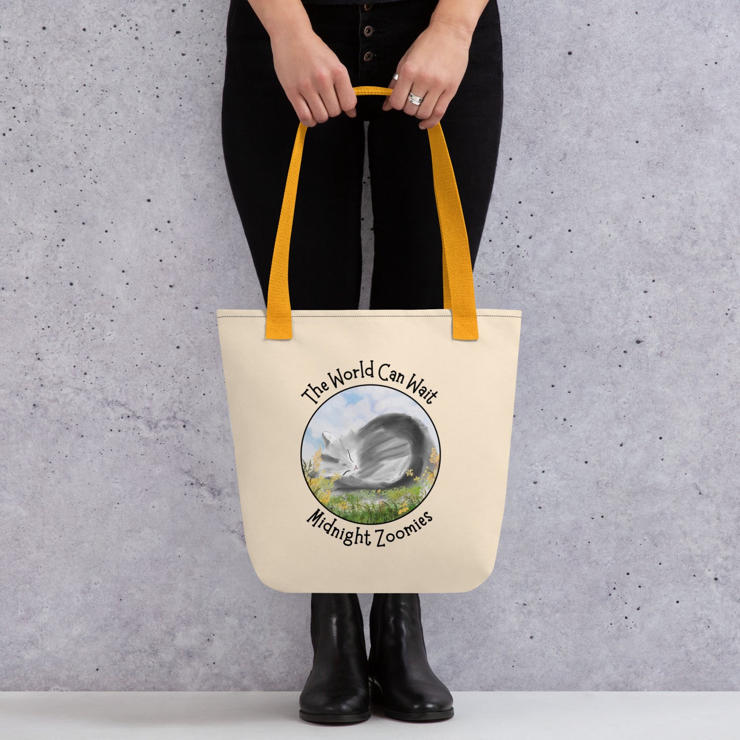 Front View of a tote bag with a design of a cat sleeping in a field of flowers with the words "The World Can Wait. Yellow Handle.